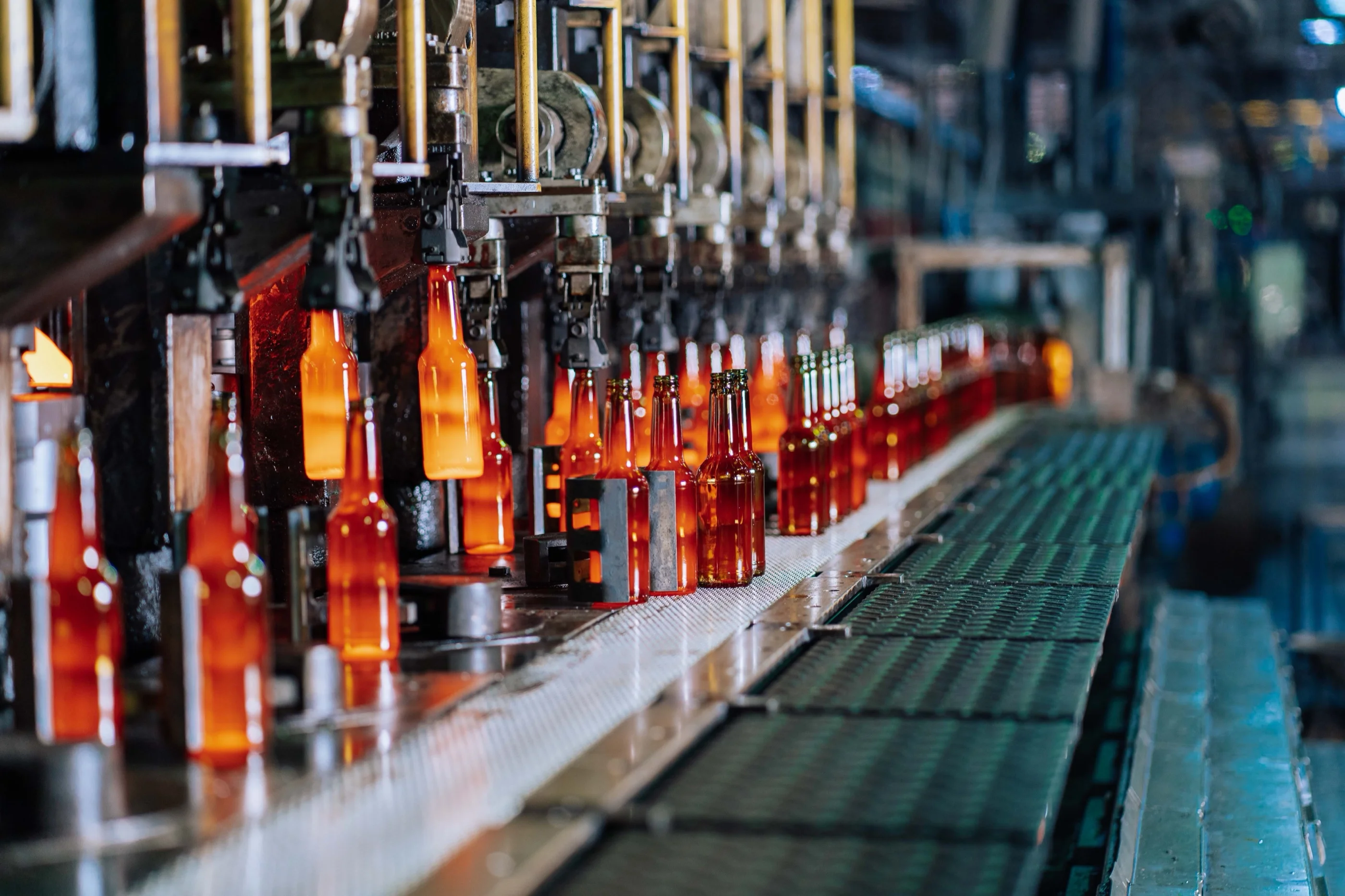 Glowing amber glass bottles fresh from the forming moulds move along a conveyor on an automated production line